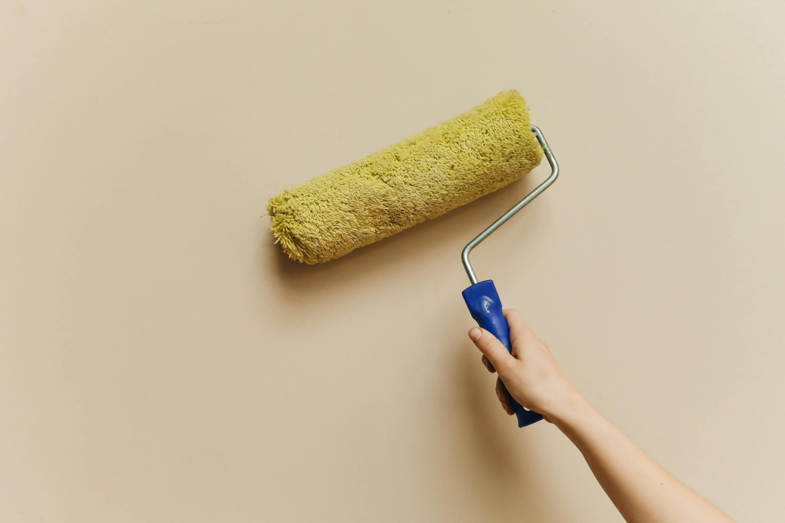 pexels photo 5583126 5583126 A hand using a yellow paint roller to paint a beige wall. Perfect for DIY and home improvement themes.